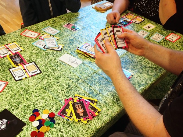 A 4-player card game in progress, with cards representing power-ups and components of cartoon robots in battle.